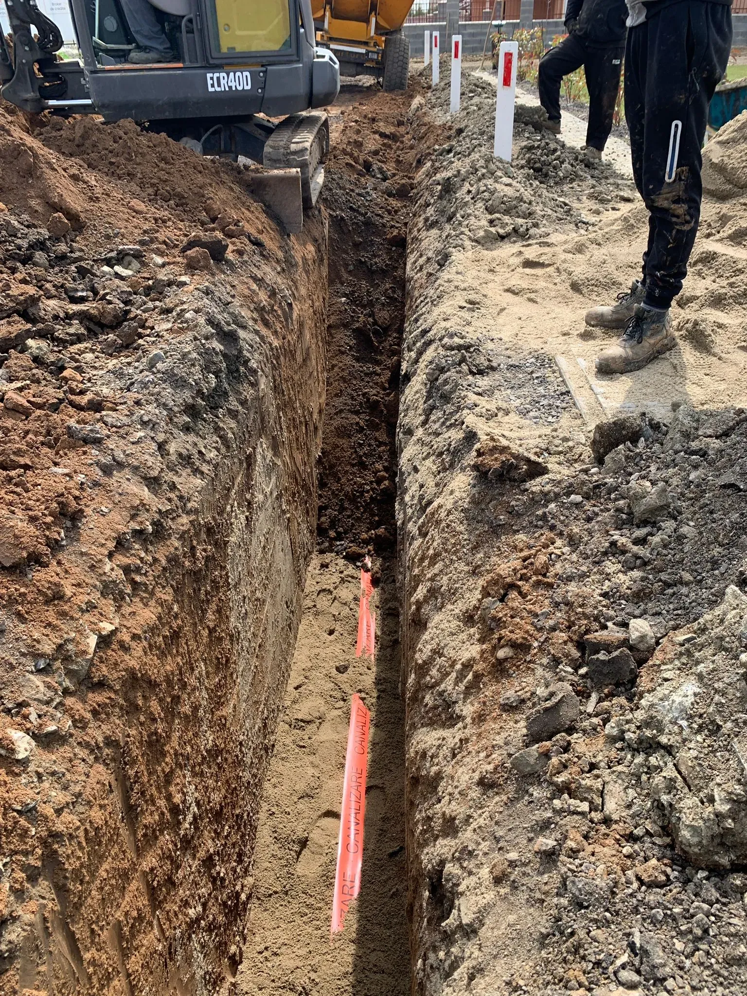 Tranșee cu tub de protecție așezat pe fund, cu excavatorul la capătul traseului